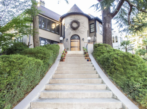 A charming house with a circular entrance, surrounded by greenery and a staircase lined with potted plants.