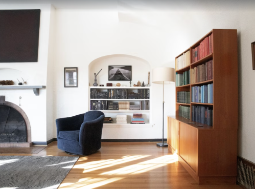 Cozy living room with a blue chair, bookshelf, and fireplace, featuring warm wood tones and minimalist decor.