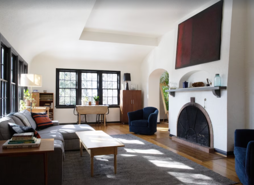 Bright, modern living room with a sofa, coffee table, and fireplace, featuring large windows and stylish decor.