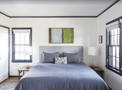 A modern bedroom featuring a large bed with gray bedding, two lamps, and abstract wall art above the headboard.