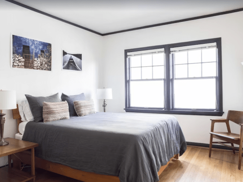 A cozy bedroom featuring a bed with gray bedding, two windows, and framed photos on the wall.