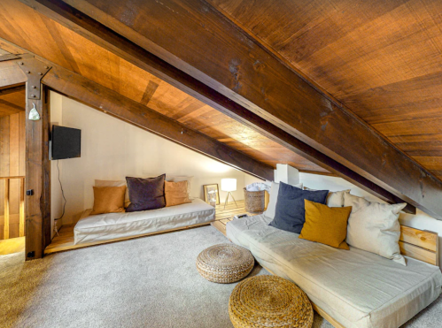Cozy attic space with sloped wooden ceilings, soft seating, decorative pillows, and warm lighting.