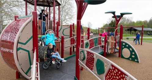 A colorful playground with children playing, featuring slides, climbing structures, and accessible areas.