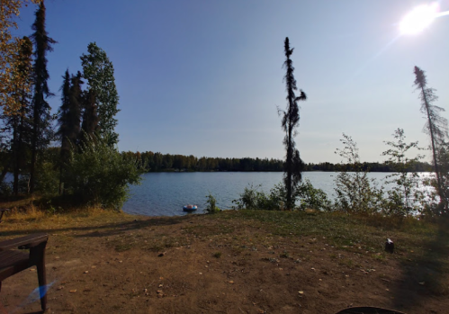 A serene lakeside view with trees, a clear sky, and a small boat on the water.
