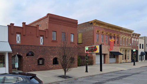A street view of two historic buildings, one with a red brick facade and the other with ornate yellow detailing.