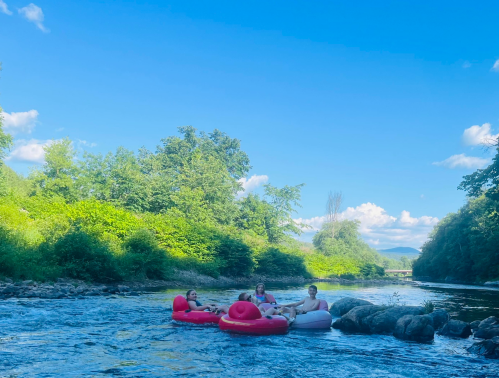 Three people relax on inflatable rafts in a river, surrounded by lush greenery and a clear blue sky.