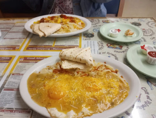 Two plates of breakfast food on a table: one with eggs, cheese, and tortillas; the other with hash browns and toppings.
