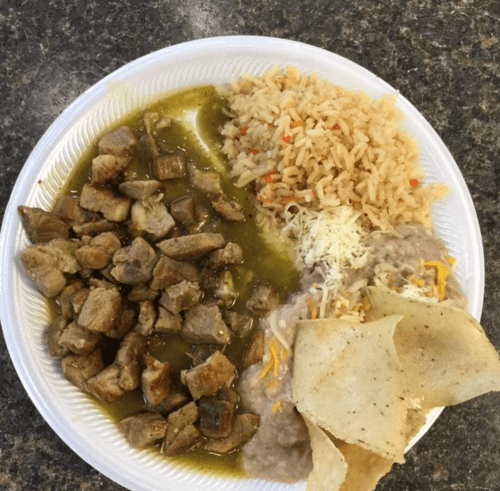 A plate of food featuring diced meat in green sauce, rice, refried beans with cheese, and tortilla chips.