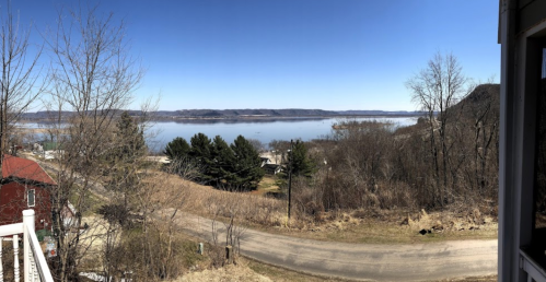 Panoramic view of a serene lake surrounded by trees and hills under a clear blue sky.