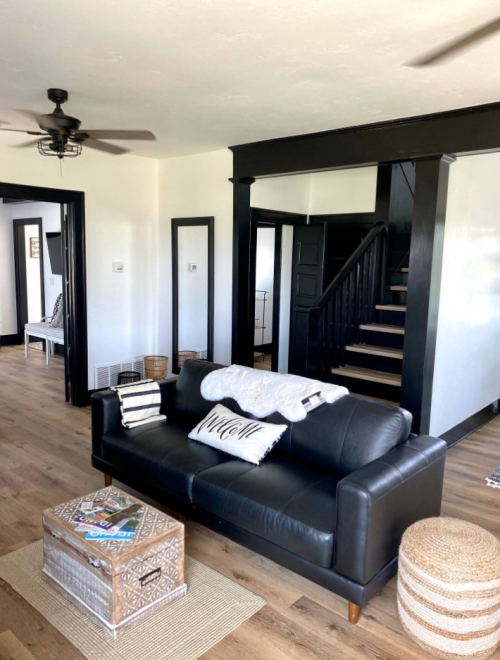 Cozy living room with a black sofa, decorative pillows, a coffee table, and a staircase in a bright, modern space.