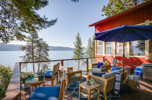 Cozy outdoor seating area with blue cushions, overlooking a serene lake and forested hills under a clear sky.