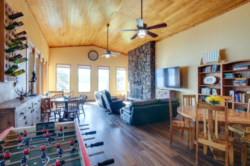 Cozy living area with a foosball table, stone fireplace, large windows, and wooden furniture.