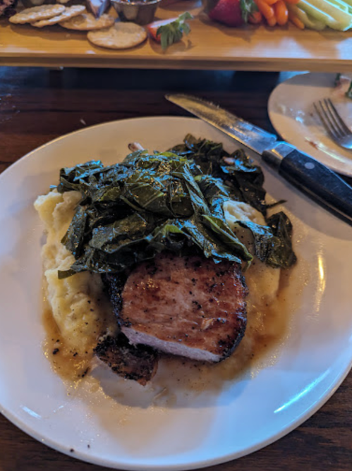 A plate of pork chop topped with collard greens, served over creamy mashed potatoes.