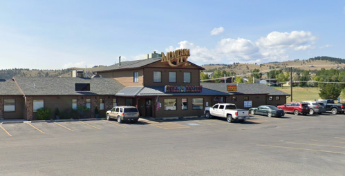 A two-story building with a sign reading "Motel" and parked cars in front, set against a hilly landscape.