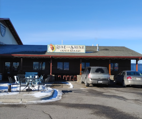 Exterior of Rise and Shine Cafe & Bakery, featuring a sign, outdoor seating, and a clear blue sky.