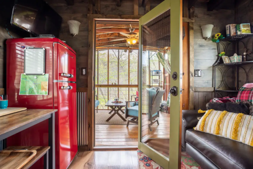 Cozy cabin interior with a red fridge, wooden decor, and a view of a screened porch with seating.