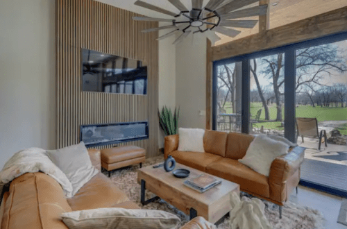 Cozy living room with leather sofas, a wooden coffee table, and large windows overlooking a green outdoor space.