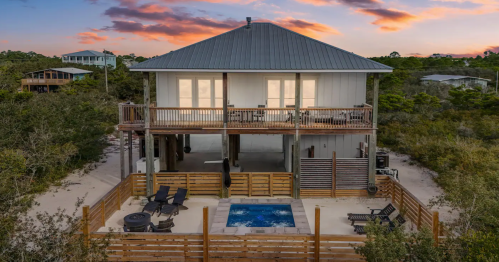 A modern beach house with a pool, surrounded by greenery, under a colorful sunset sky.