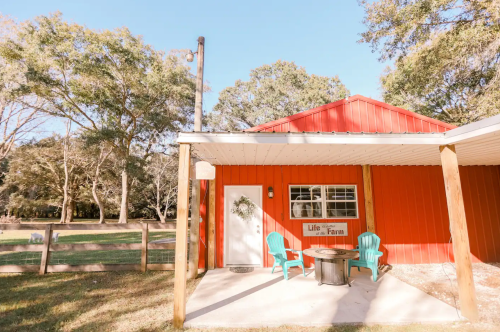 A cozy red farmhouse with a porch, featuring two teal chairs and a sign that reads "Life on the Farm."