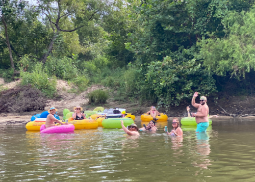 A group of people enjoying a summer day in colorful inner tubes on a river, surrounded by greenery.