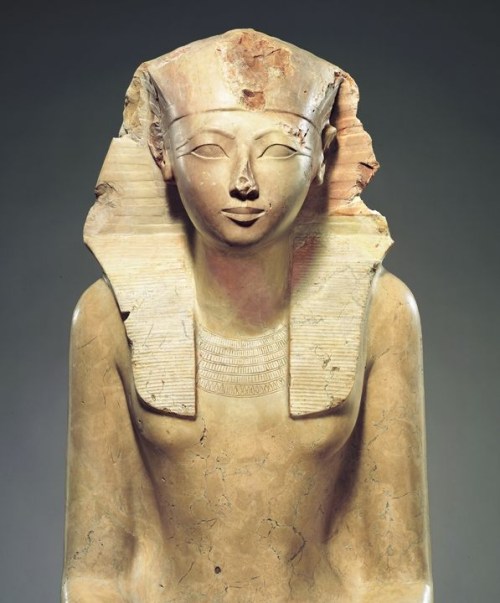 Ancient Egyptian statue of a woman with a headdress, featuring detailed facial features and a smooth, polished surface.