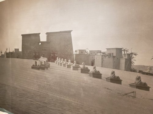 Black and white photo of ancient Egyptian structures with statues lined up in front, set against a desert backdrop.
