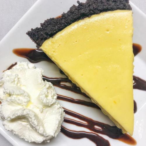 A slice of lemon pie on a plate, with whipped cream and chocolate drizzle beside it.