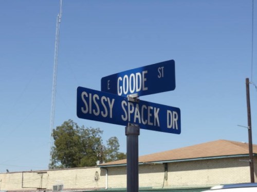 Street sign at the intersection of Goode St and Sissy Spacek Dr under a clear blue sky.