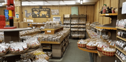 A cozy shop filled with shelves of various packaged nuts and snacks, featuring wooden decor and baskets.