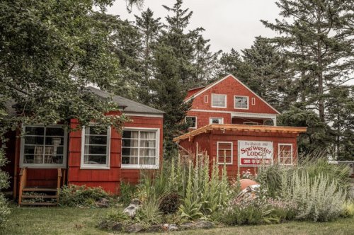 A charming red lodge surrounded by greenery, featuring two smaller red buildings and a sign for "Soul Wister Lodge."
