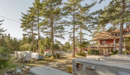 A scenic view of vintage trailers surrounded by tall trees and a rustic building in a tranquil outdoor setting.