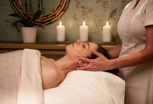 A woman receives a relaxing head massage in a serene spa setting with candles lit in the background.