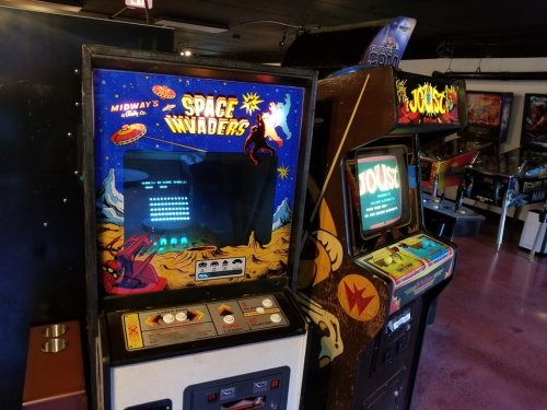 Two vintage arcade machines: "Space Invaders" and "Joust," set in a retro gaming environment.