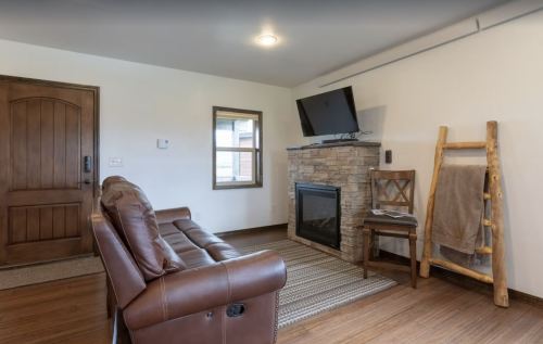 Cozy living room with a brown leather sofa, stone fireplace, TV, and wooden ladder holding a blanket.