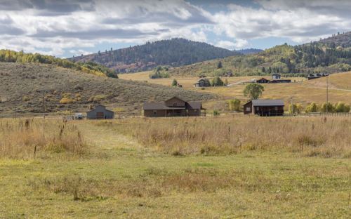 A scenic landscape featuring rolling hills, a few houses, and a cloudy sky in a rural setting.