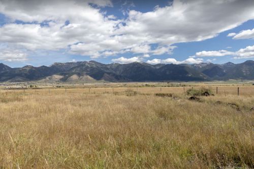 A wide view of a grassy field with mountains in the background under a partly cloudy sky.