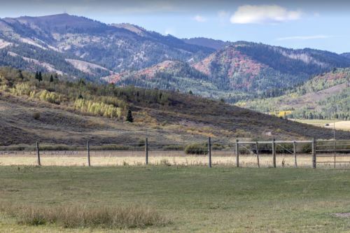 A scenic view of rolling hills and mountains, with a grassy field and a wooden fence in the foreground.