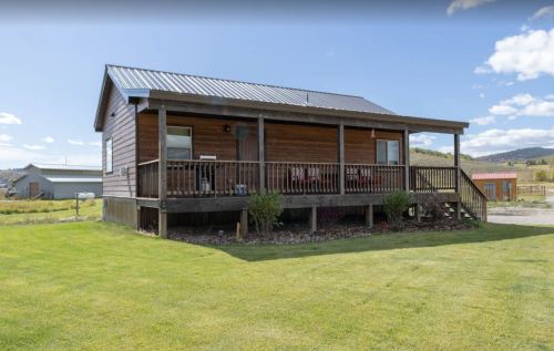 A wooden cabin with a porch, surrounded by green grass and a clear blue sky.
