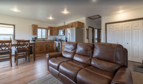 Cozy kitchen and living area featuring a leather couch, wooden cabinets, and dining table with chairs.