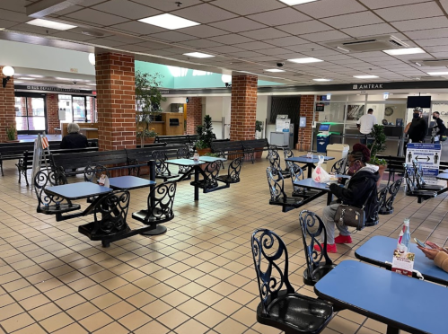 A spacious waiting area with tables and chairs, featuring brick walls and a few people seated. Amtrak signage visible.