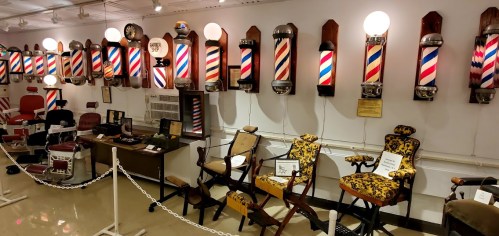 A vintage barber shop display featuring striped pole lights and various antique barber chairs.
