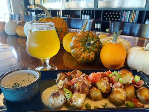 A plate of cheesy potato bites with bacon and tomatoes, paired with a glass of beer, and surrounded by decorative pumpkins.
