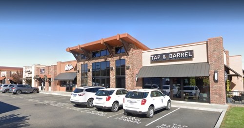 Exterior view of a restaurant called "Tap & Barrel" with parked cars in front and a clear blue sky.