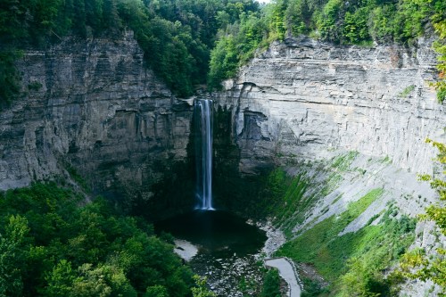 A stunning waterfall cascades into a deep gorge surrounded by lush greenery and rocky cliffs.