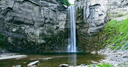 A serene waterfall cascading down rocky cliffs into a calm pool, surrounded by lush greenery.