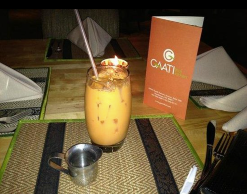 A glass of iced tea with a straw, a small metal pitcher, and a menu on a table set for dining.