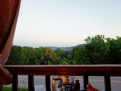A scenic view from a balcony, featuring mountains and trees at dusk, with a candlelit table in the foreground.