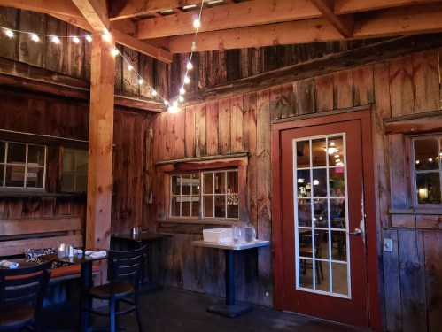 Cozy restaurant interior with wooden walls, string lights, and a door leading to another area.