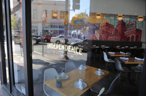 A restaurant window displays "The Independence" with a colorful mural and neatly set tables inside.