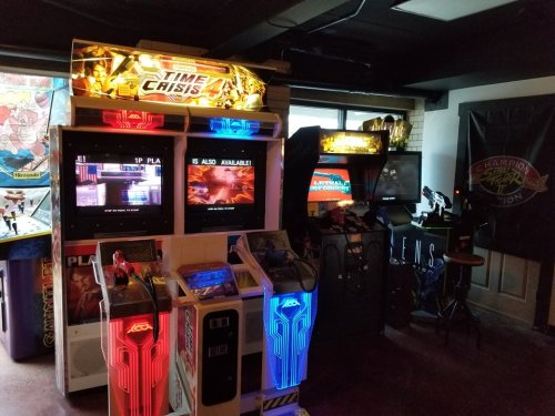 A cozy arcade room featuring classic game machines, including "Time Crisis," with colorful screens and retro decor.